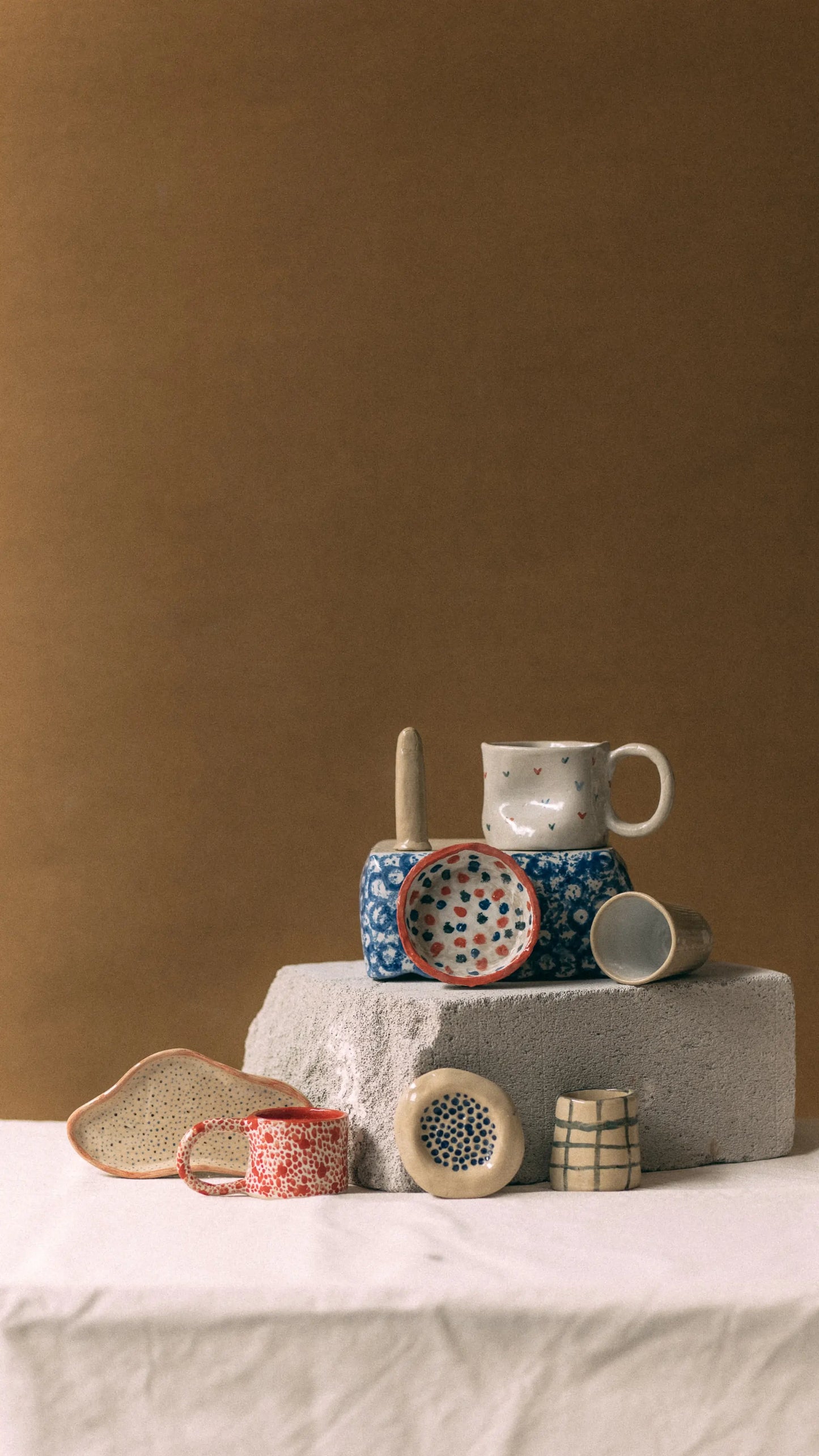 Kolekcja kolorowych ręcznie robionych ceramicznych kubków, misek i naczyń z malowanymi wzorami wystawionych na betonowych blokach - voucher miesięczny kurs lepienia 4 spotkania