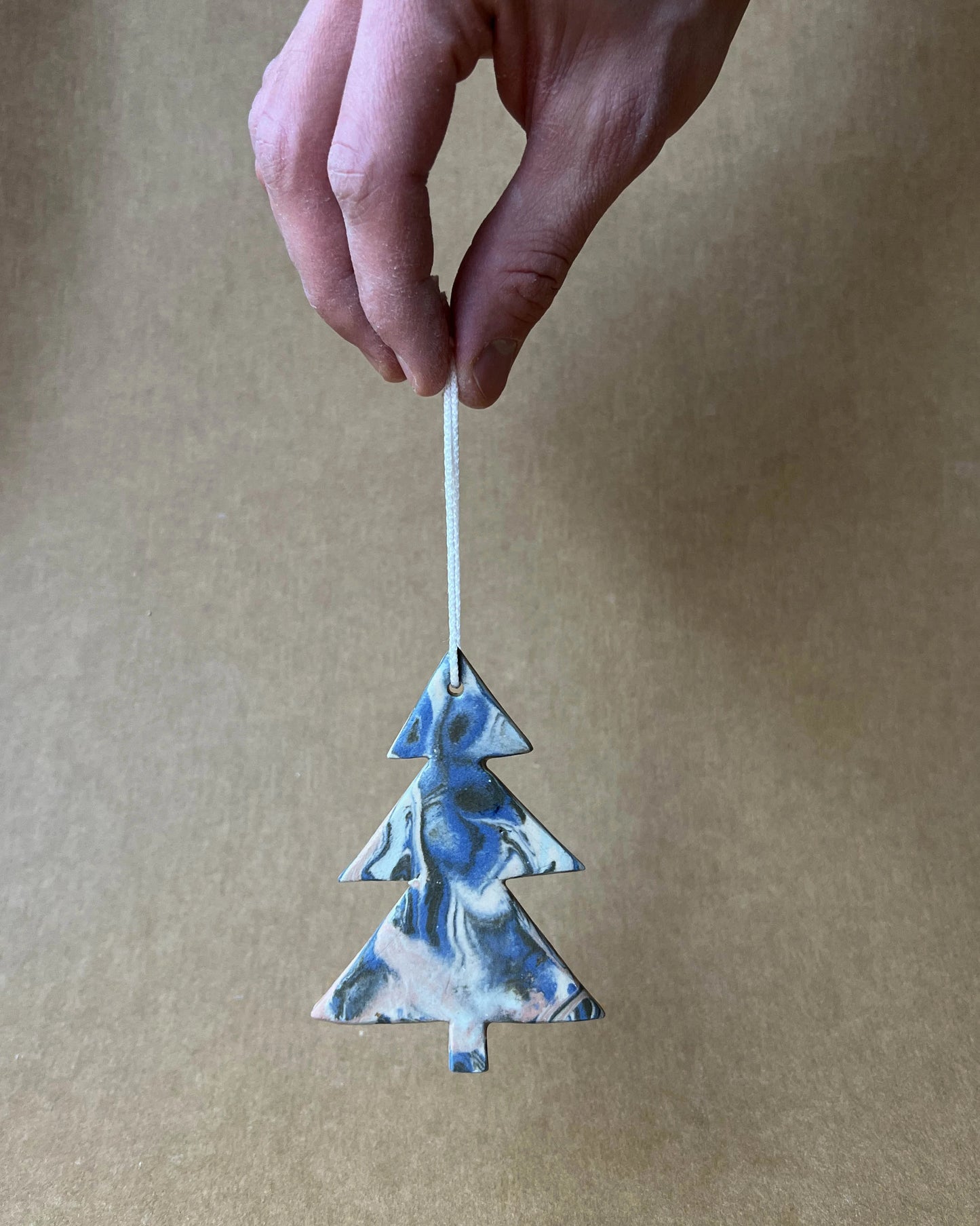 Ręka trzymająca za sznurek zawieszkę w kształcie choinki, wykonaną z organicznie połączonych ze sobą kolorowych mas