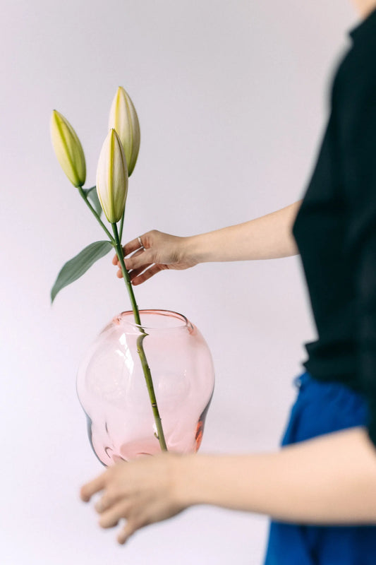 Dłonie wkładające białą lilię do różowego, szklanego wazonu Ganna Glass - delikatny odcień brzoskwiniowy