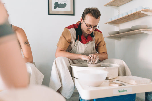 Uśmiechnięty uczestnik warsztatu garncarskiego Zakwas Studio toczący ceramikę na kole