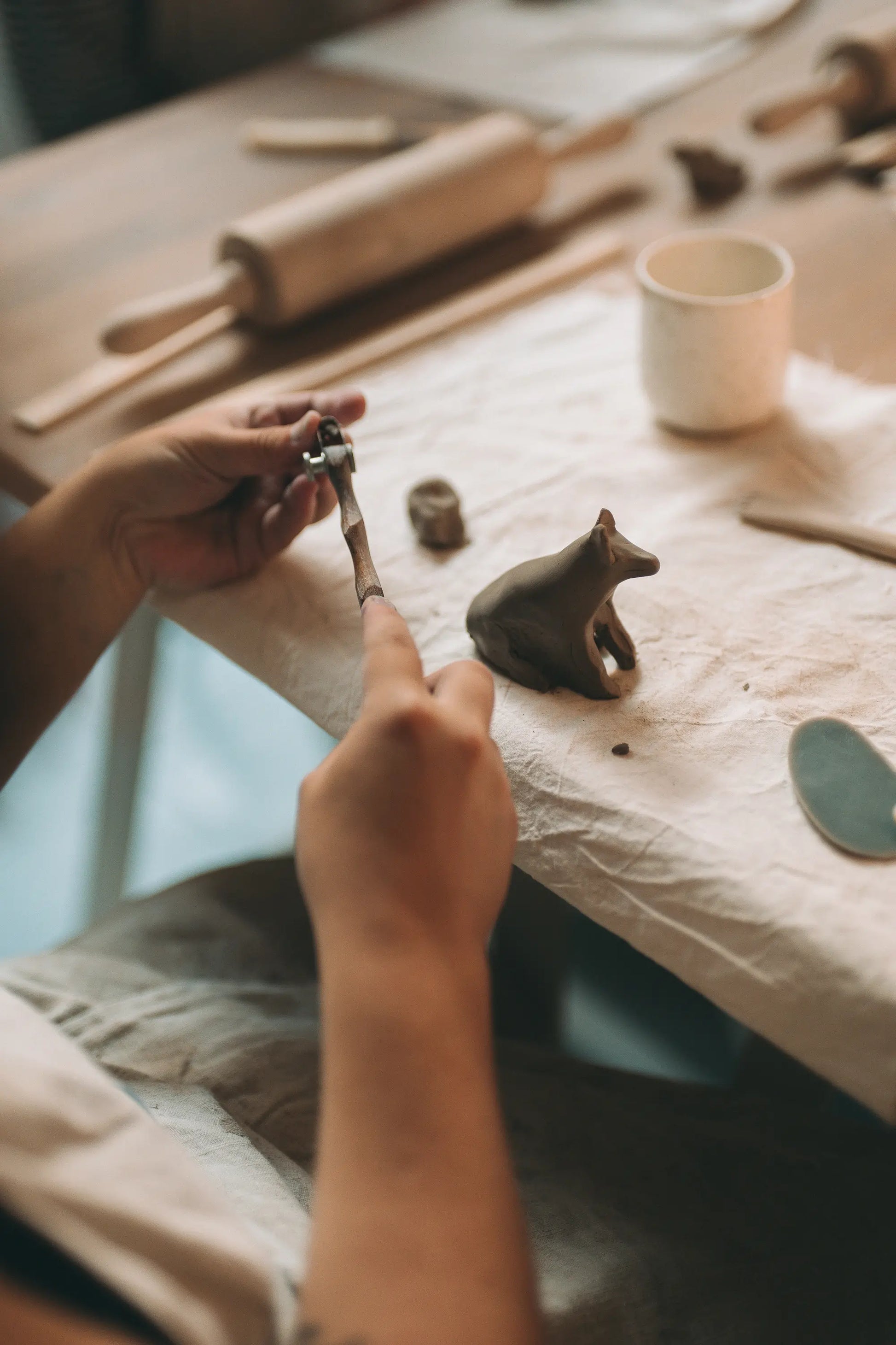 Ręce lepiące ceramiczną figurkę zwierzęcia narzędziami garncarskimi przy stole warsztatowym - voucher skrócony kurs lepienia 2 spotkania