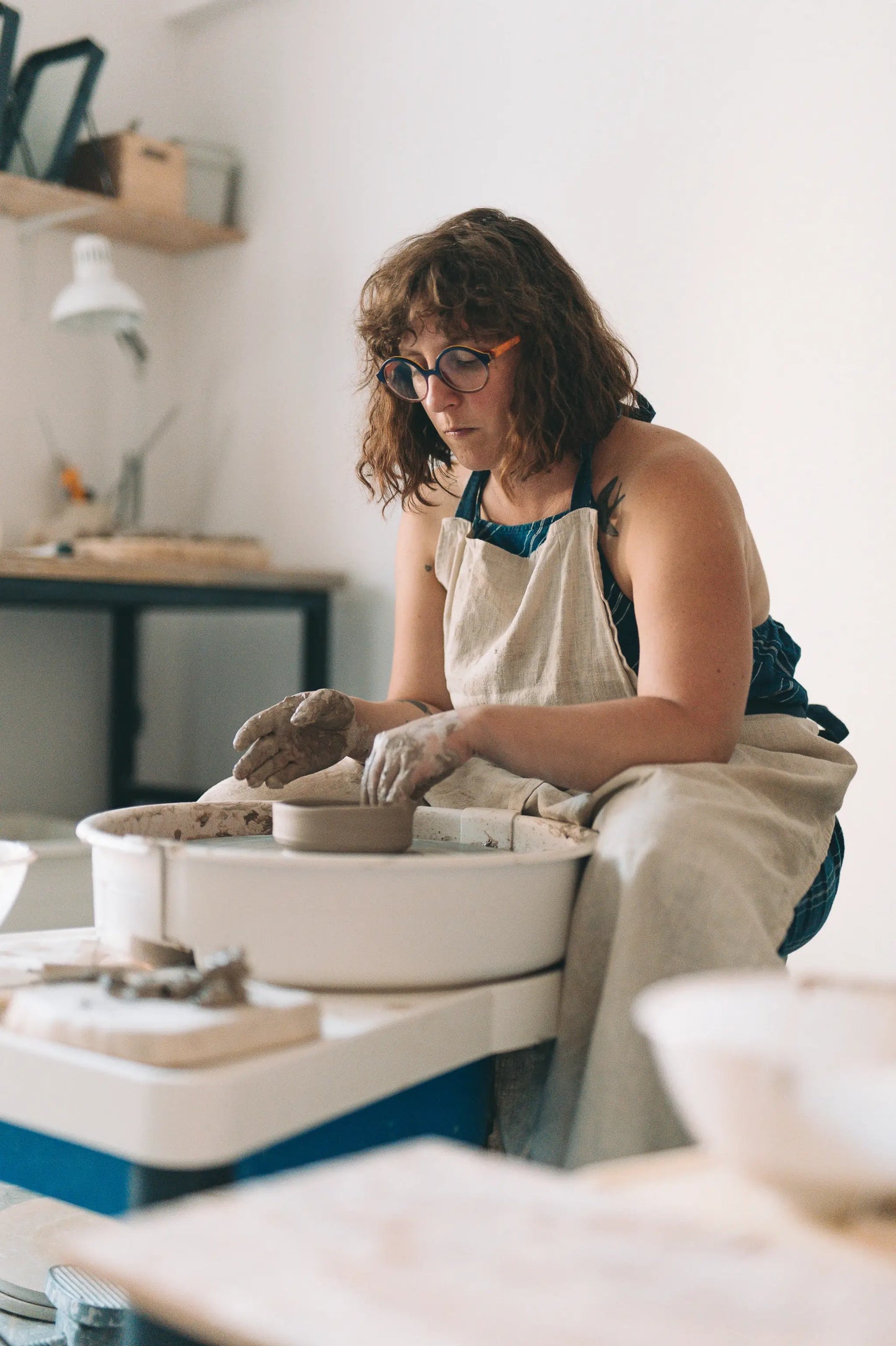 Kobieta w okularach i fartuchu centrowująca glinę na kole garncarskim w Zakwas Studio - voucher Koło na start 1 spotkanie