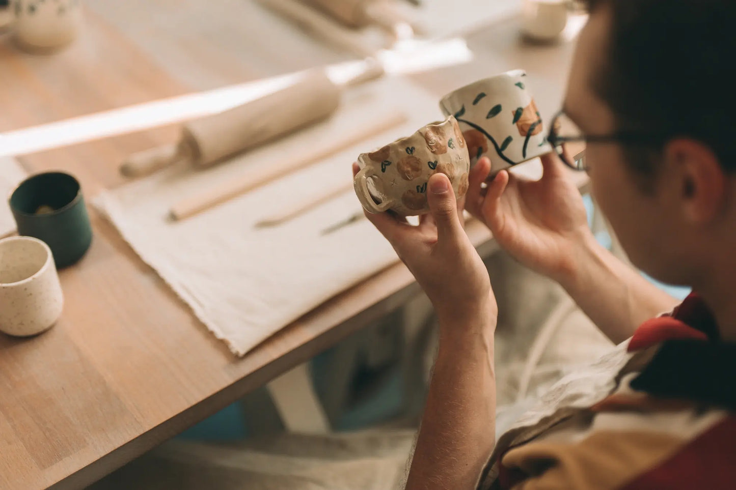 Warsztatowe ujęcie dłoni trzymających ceramiczne naczynie kubki przy stole z narzędziami - voucher skrócony kurs lepienia 2 spotkania