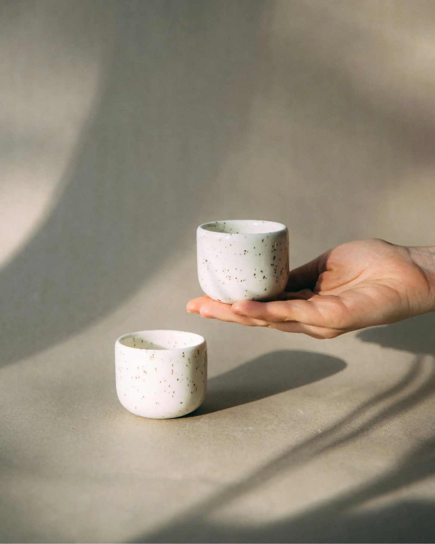 Dłoń podtrzymuje duet białych czarek ceramicznych PopUp 80ml na jasnym tle