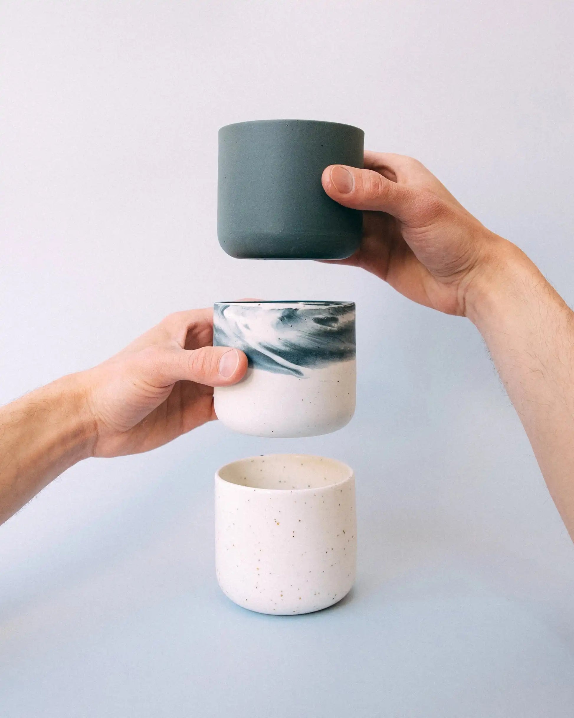 Dłonie trzymające kubki ceramiczne TAP w kolorach białym, grafitowym i biało-grafitowym