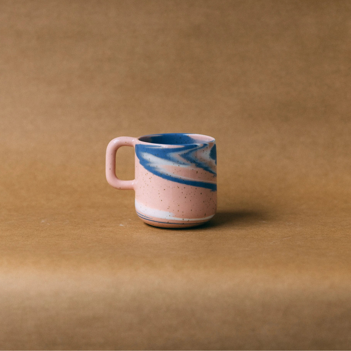 Kubek ceramiczny z uchem Niebko, różowo-niebiesko-biały, ustawiony na jasno brązowym tle - widok z boku