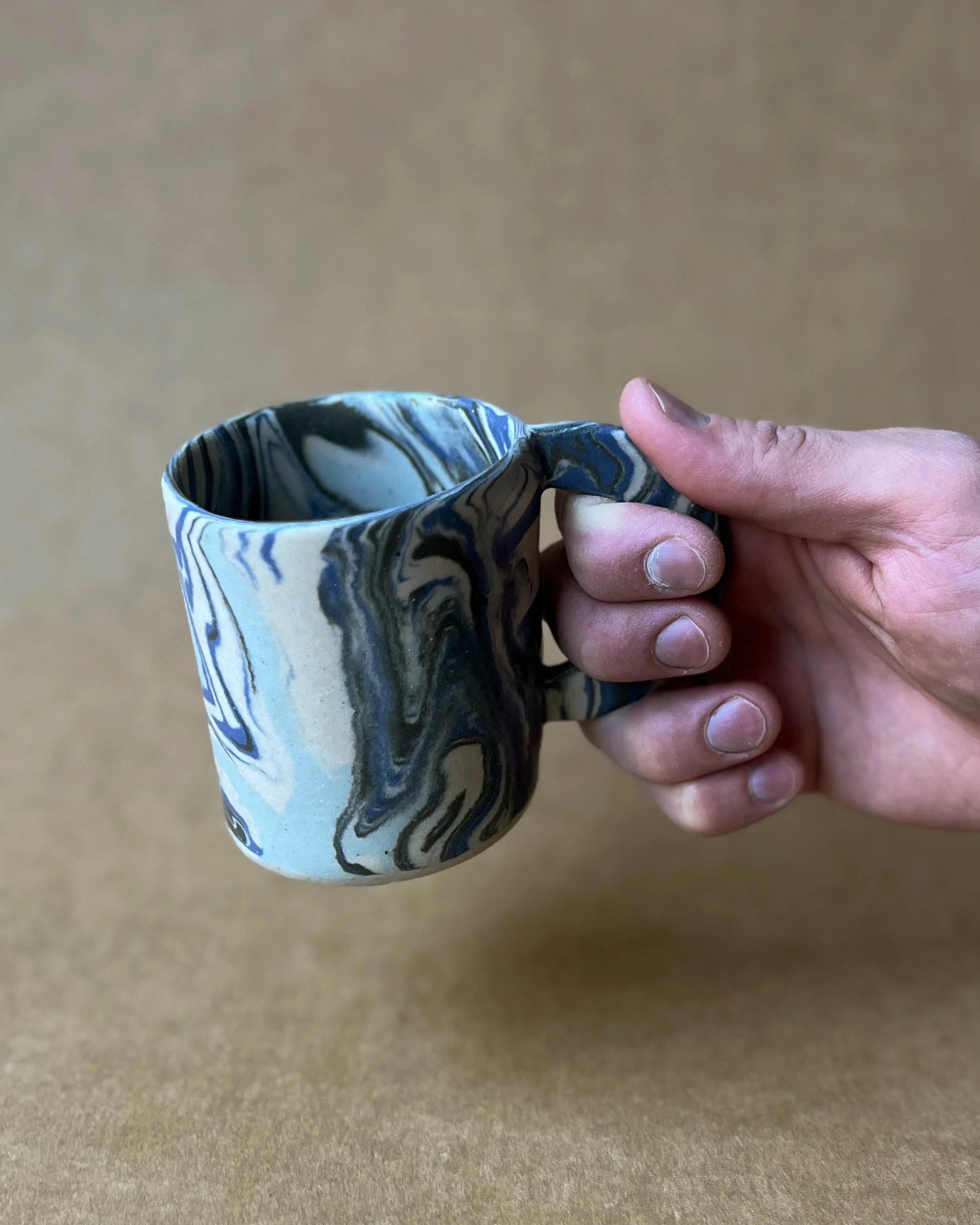 Ręka trzymająca za ucho kubek ręcznie wykonany z organicznie zmieszanych ze sobą różnokolorowych glin