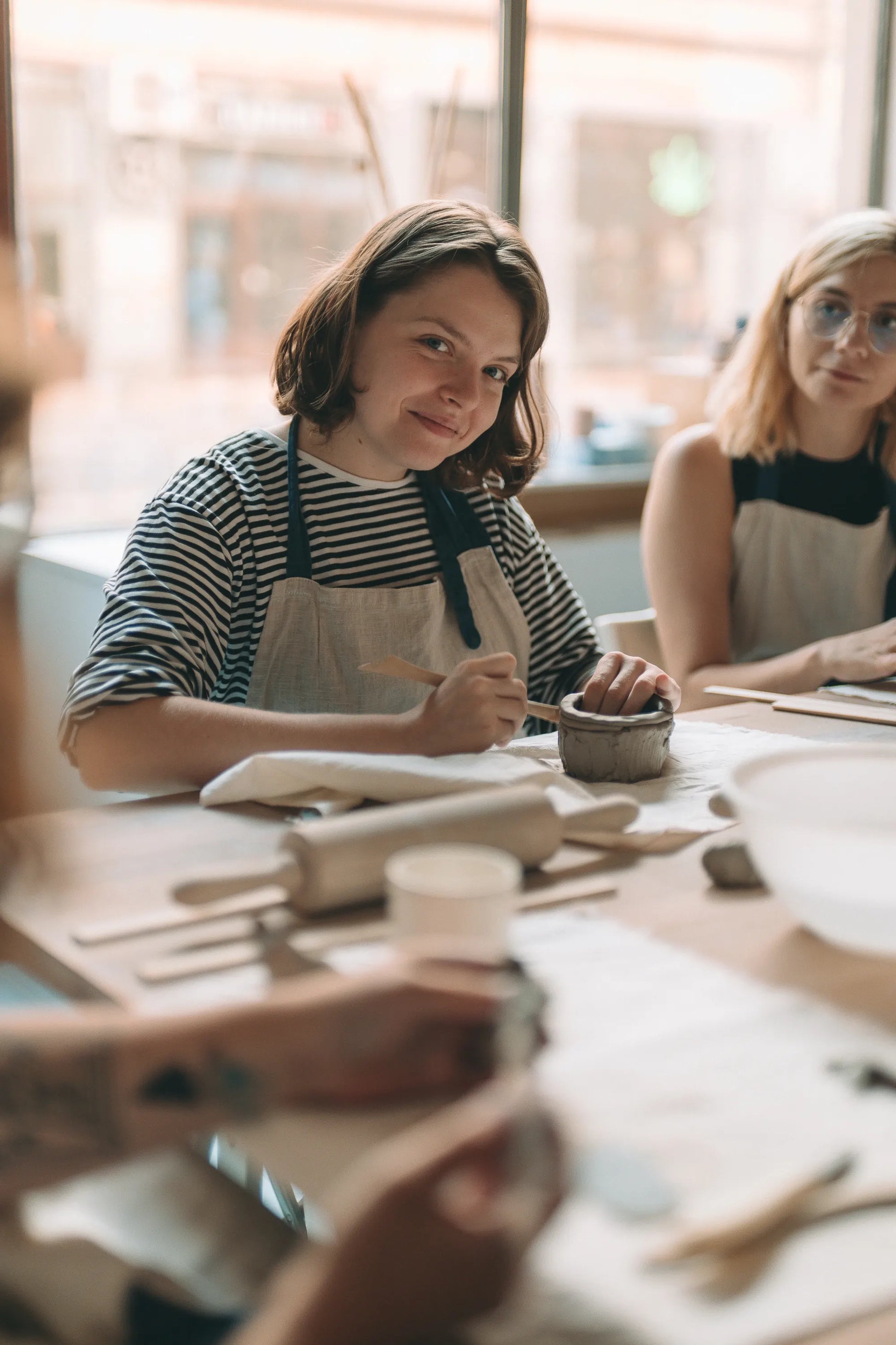 Uczestniczka w pasiastej koszulce lepiąca ceramiczną miskę podczas miesięcznego kursu ceramiki w Zakwas Studio