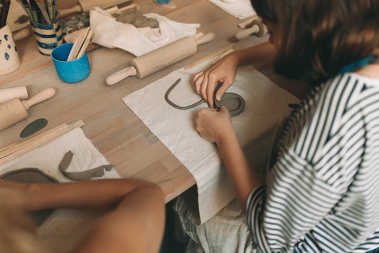 Widok z góry na uczestników warsztatu ceramicznego lepiących glinę wałkami i narzędziami do modelowania