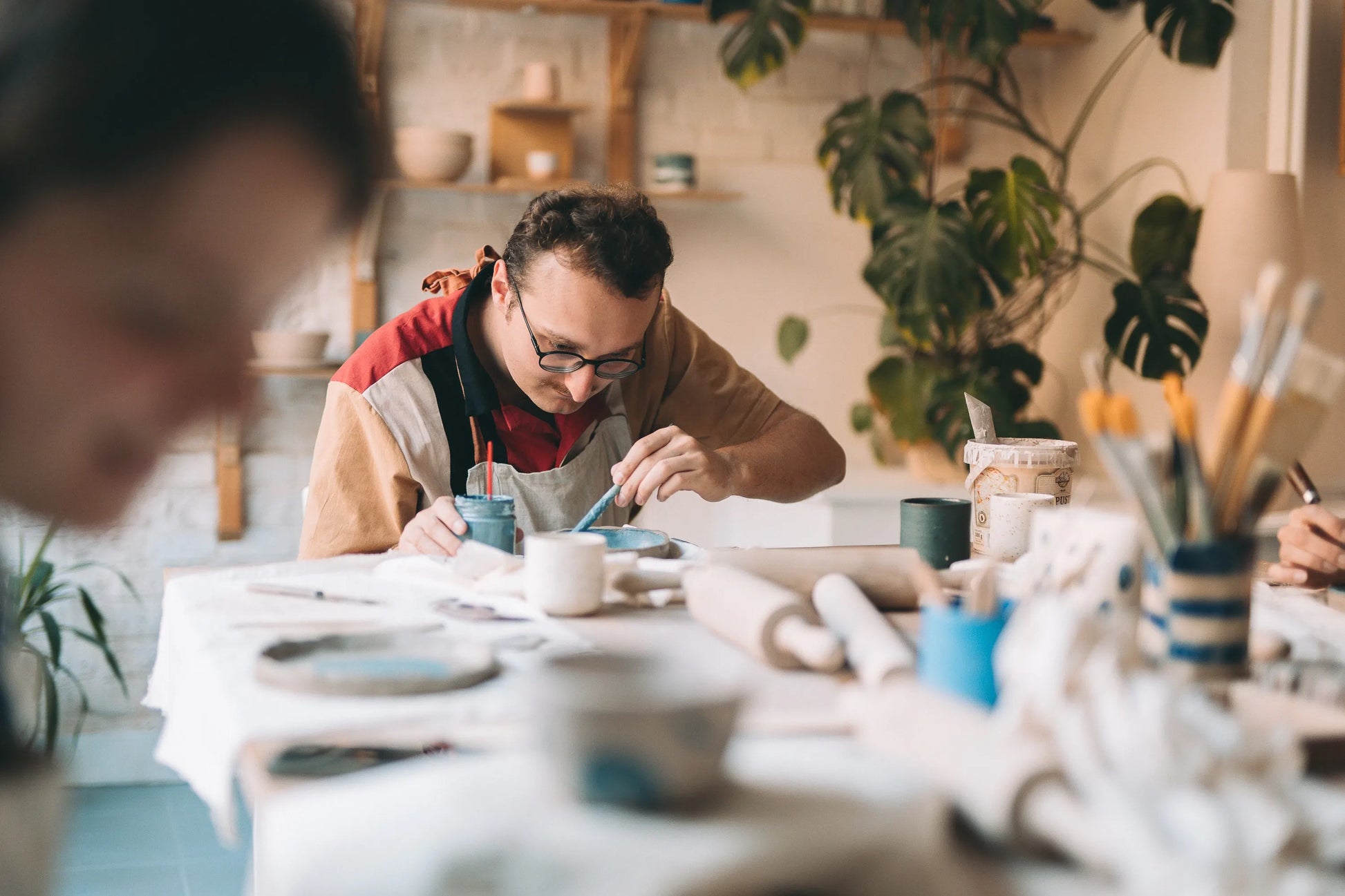Uczestnik warsztatów ceramiki malujący dekoracyjny talerz w pracowni otoczonej roślinami i narzędziami