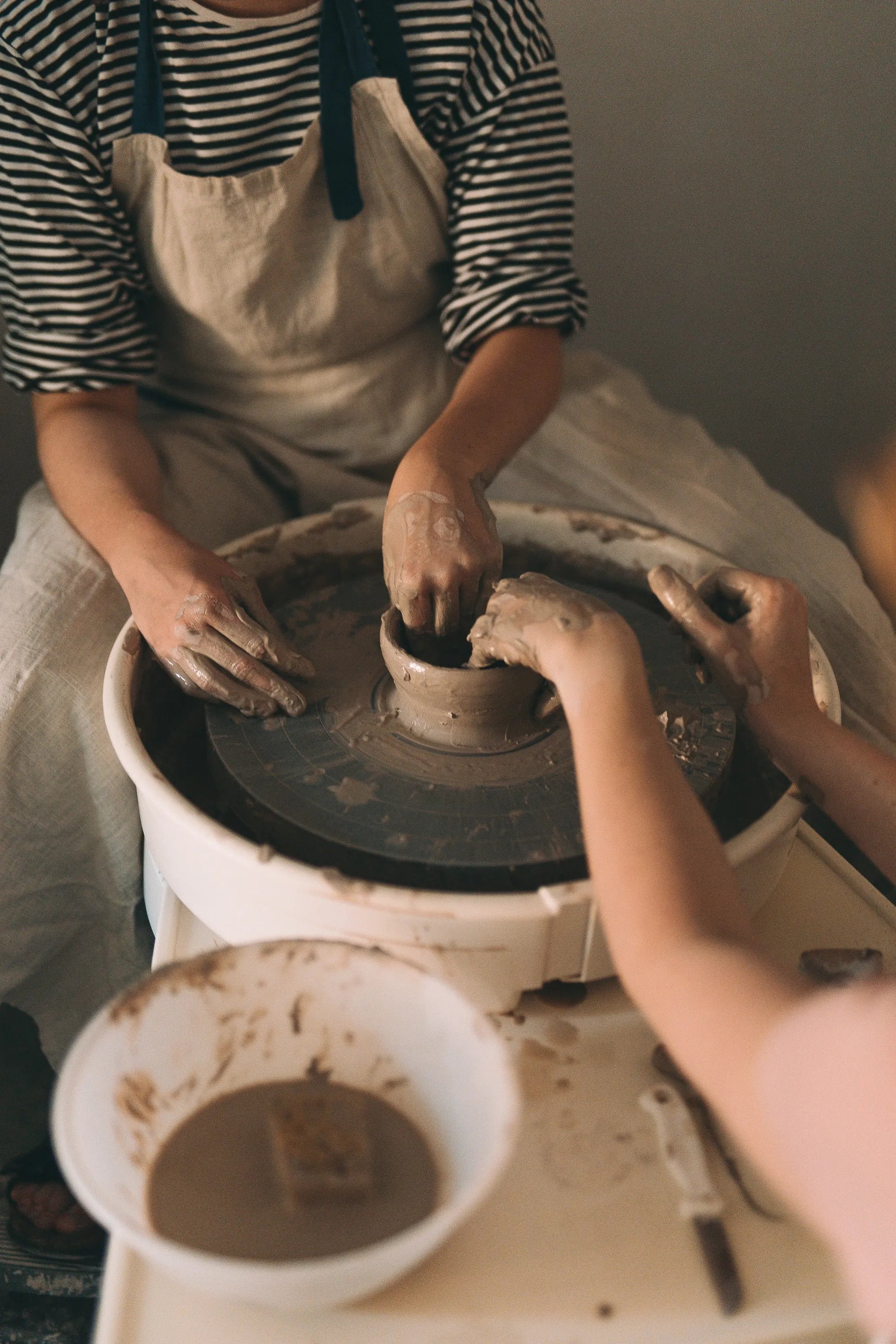 Dwie pary rąk pracujące na kole garncarskim