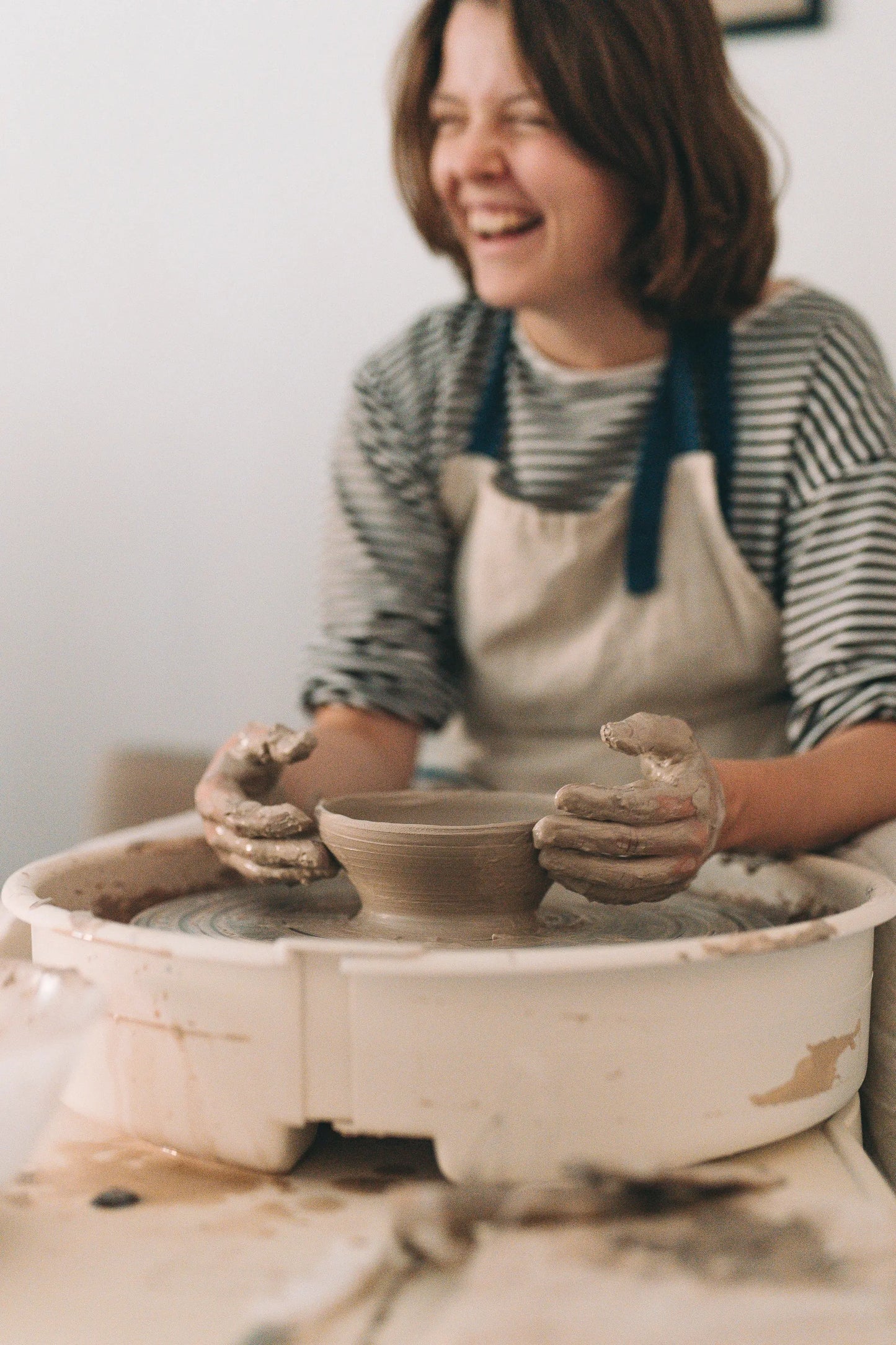 Zbliżenie na uśmiechniętą uczestniczkę warsztatu i jej dłonie całe w glinie po pracy na kole - miesięczny kurs garncarski