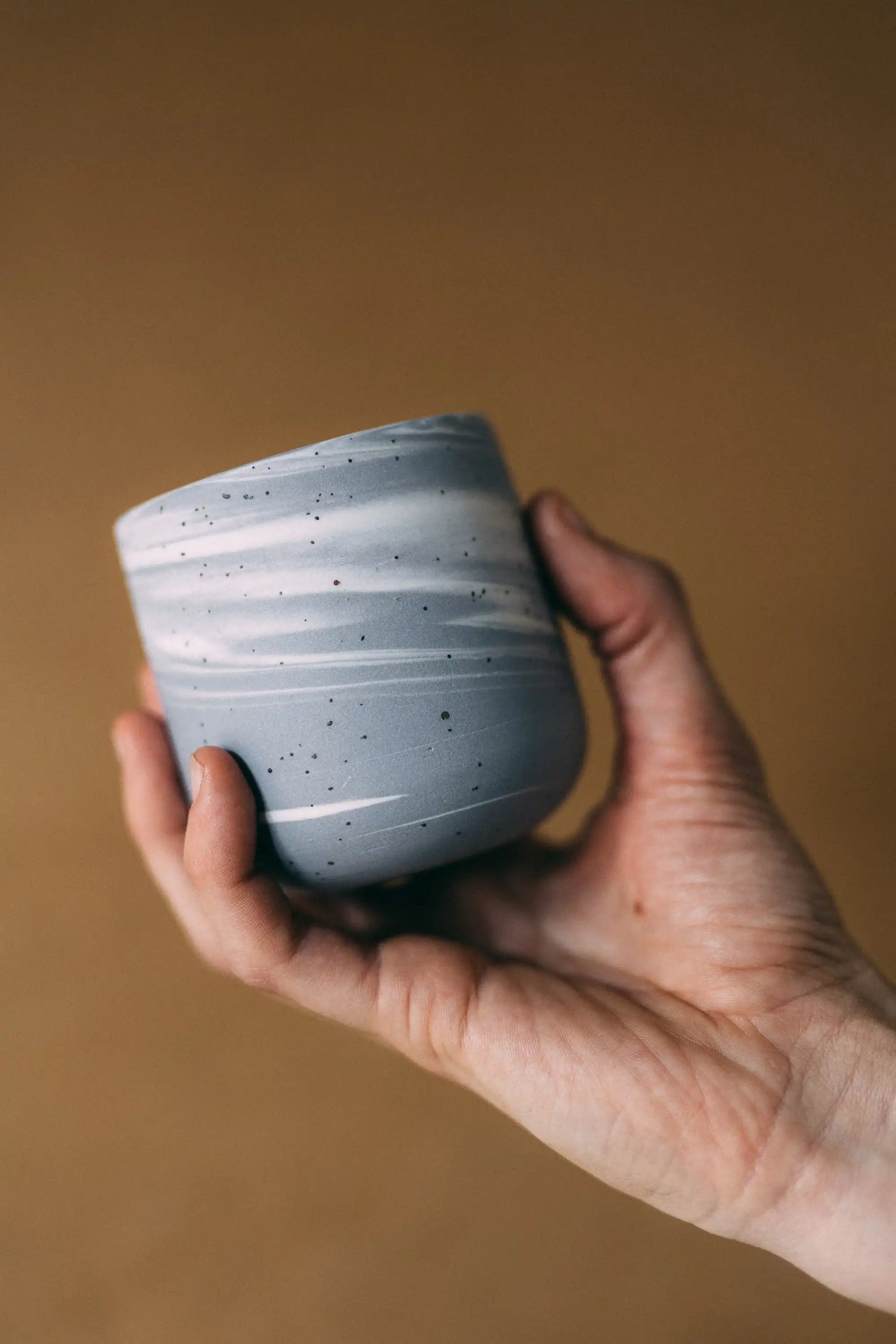 Dłoń prezentująca czarkę ceramiczną PopUp BRZASK w marmurkowym kolorze szaro-białym