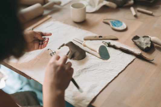 Dłonie lepiące małą figurkę z gliny narzędziami garncarskimi podczas skróconego kursu ceramiki