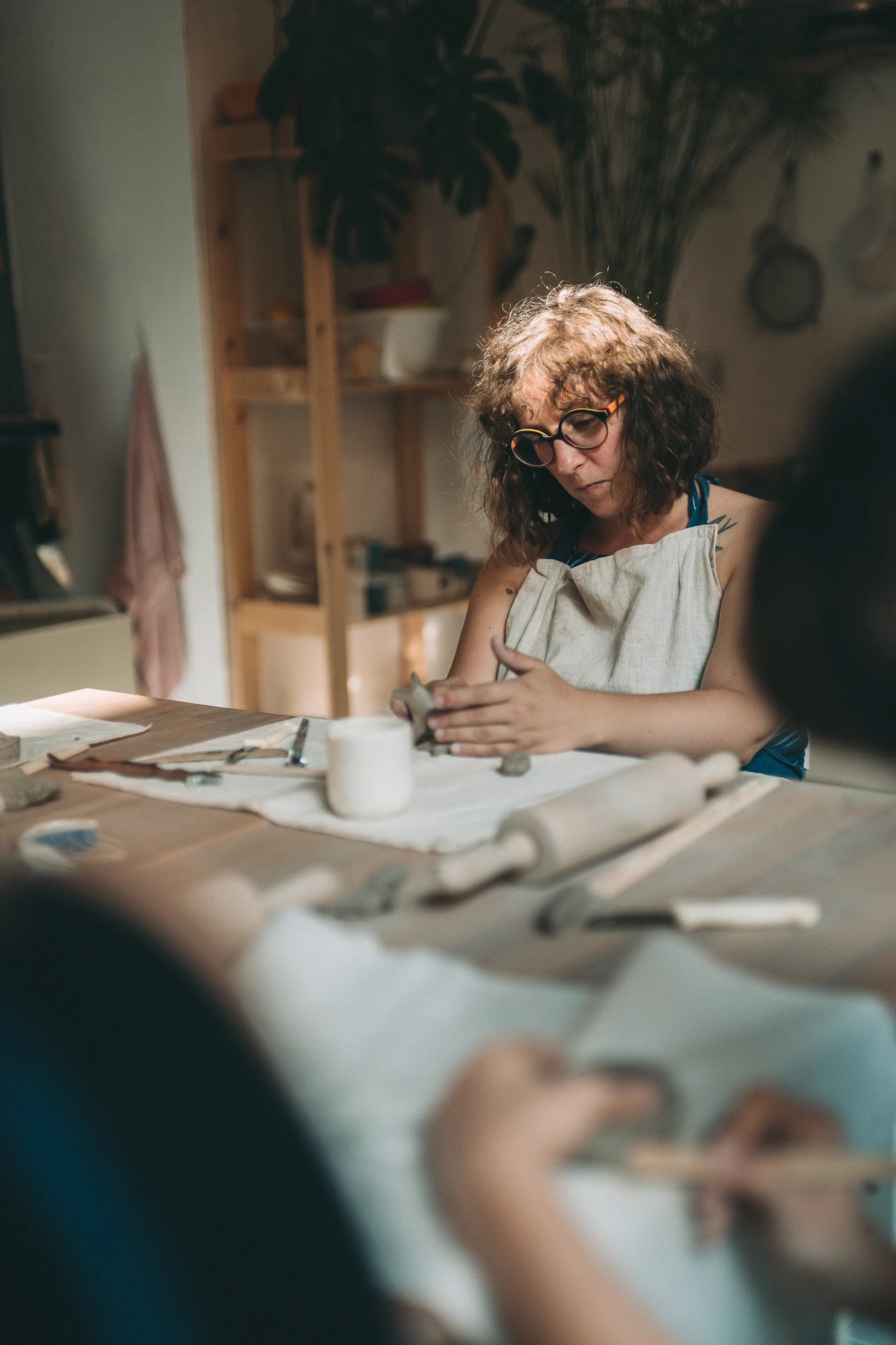 Uczestniczka warsztatów pracująca nad glinianymi elementami przy stole warsztatowym podczas kursu lepienia
