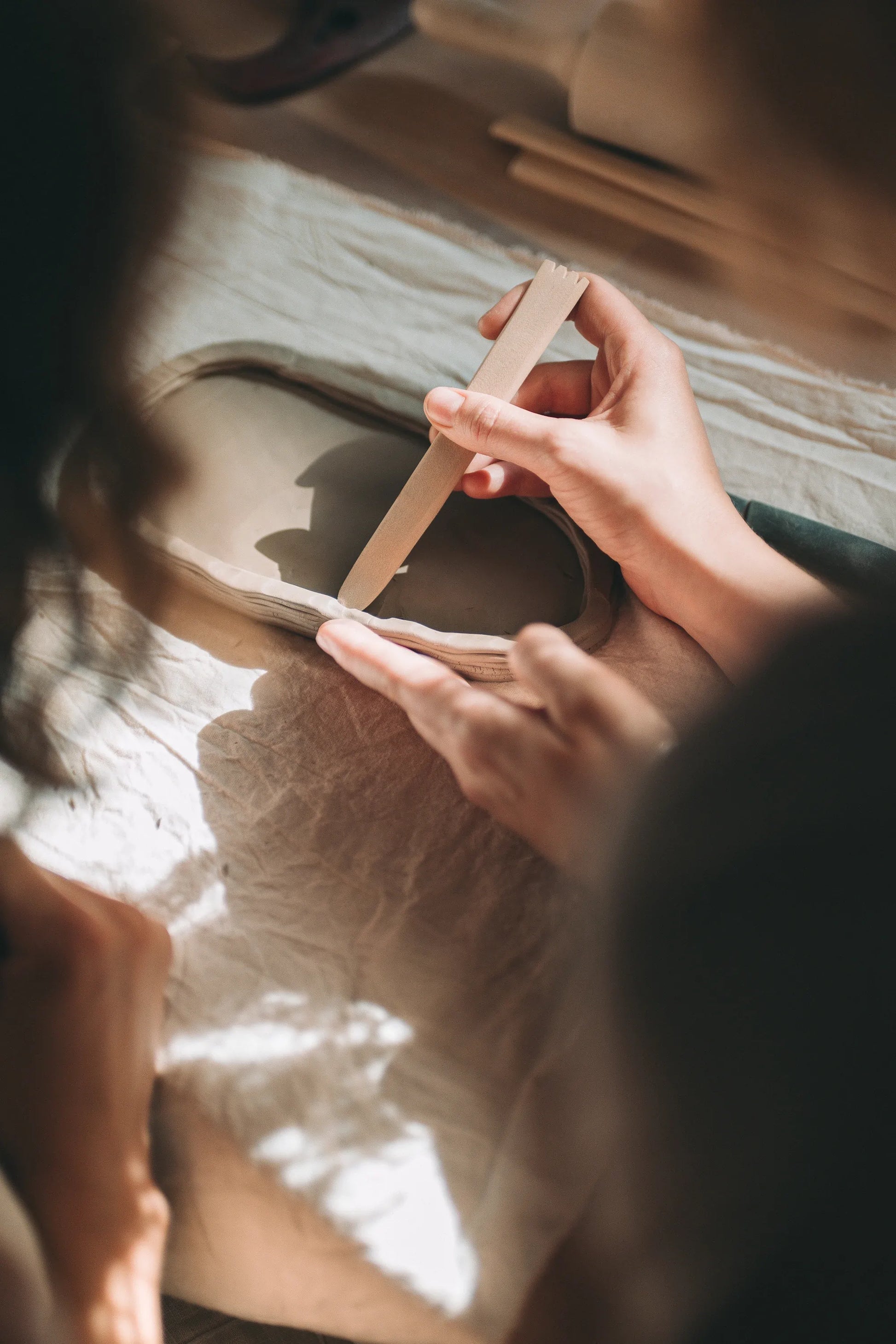 Zbliżenie na dłonie wygładzające ceramiczną miskę drewnianym narzędziem podczas warsztatu podstawowych technik lepienia