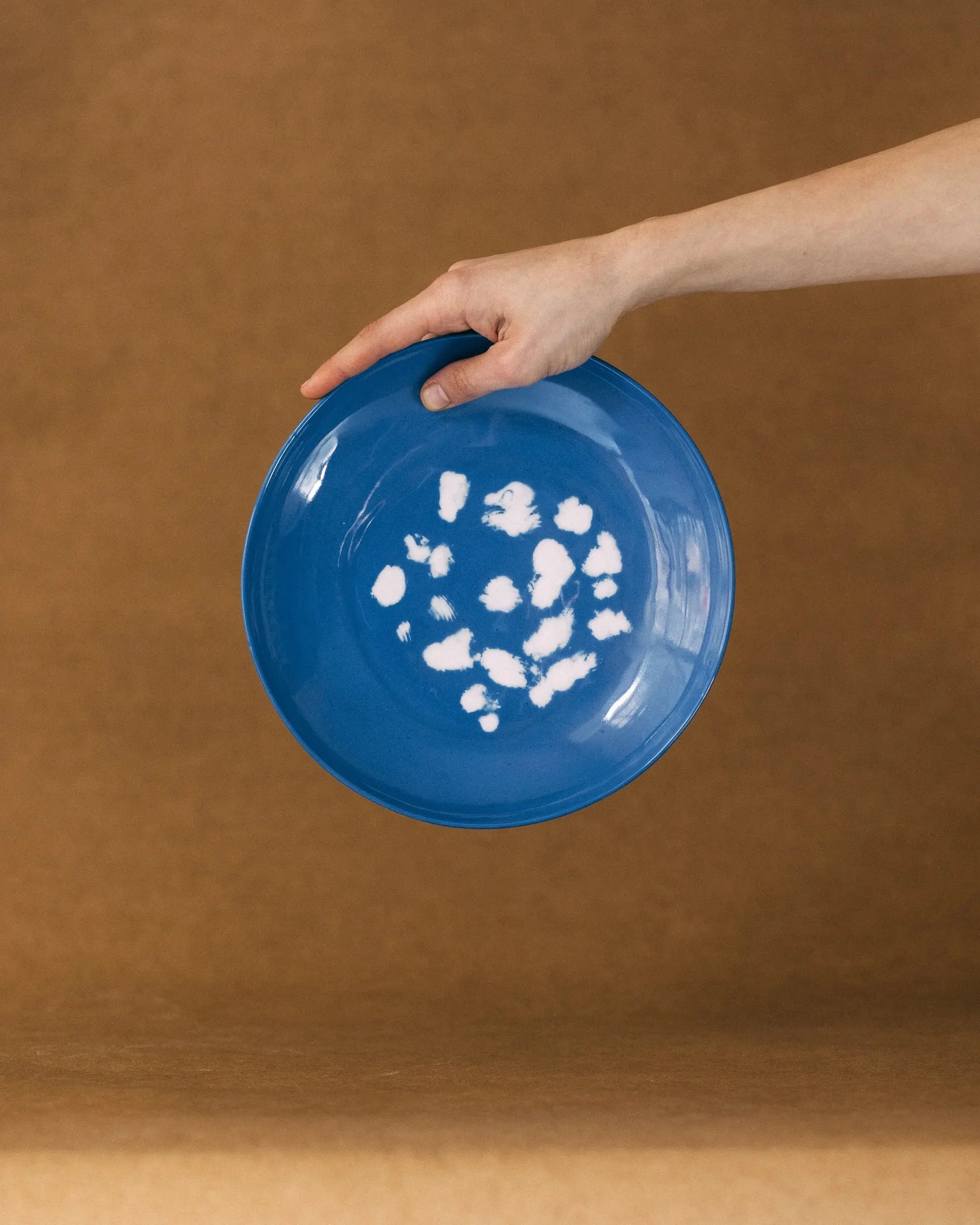 Dłoń trzymająca niebieski, okrągły talerz w białe, nieregularne wzory przypominające kropki