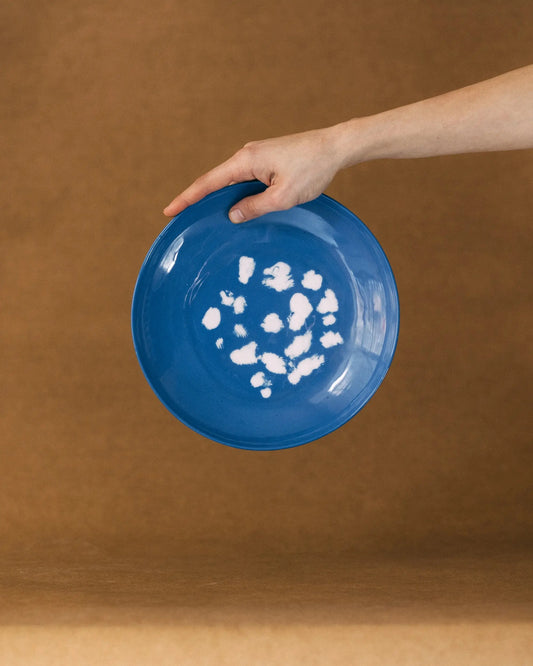 Dłoń trzymająca niebieski, okrągły talerz w białe, nieregularne wzory przypominające kropki