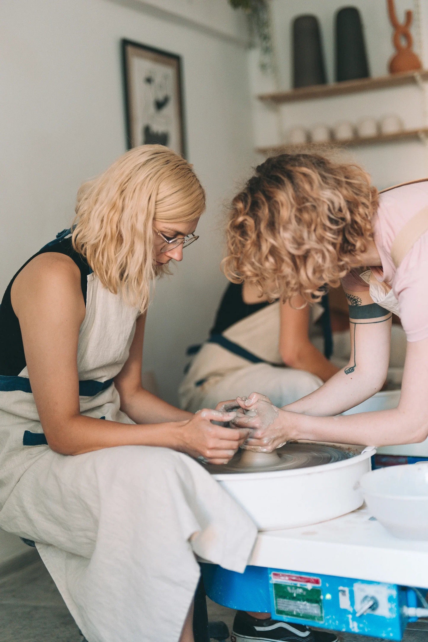 Uczestniczka warsztatów garncarskich, wraz z prowadzącą warsztaty, skupione na pracy z gliną przy kole w jasnej pracowni - miesięczny kurs garncarski