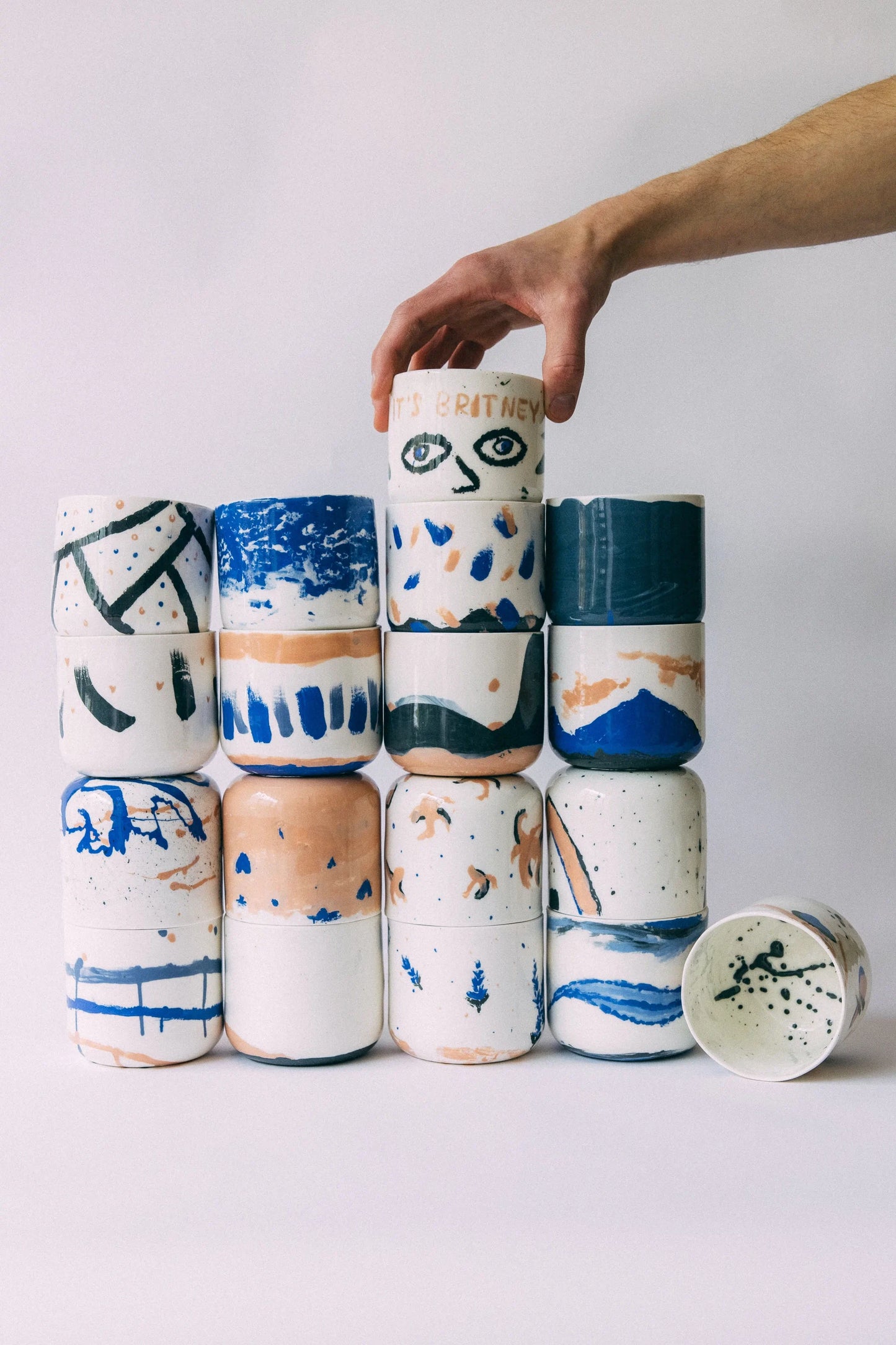 Ręka ustawiająca cylindryczny kubek z oryginalnym wzorem na wystawie porcelanowych kubków, na kształt wieży, z różnymi wzorami - warsztat odlewania porcelany