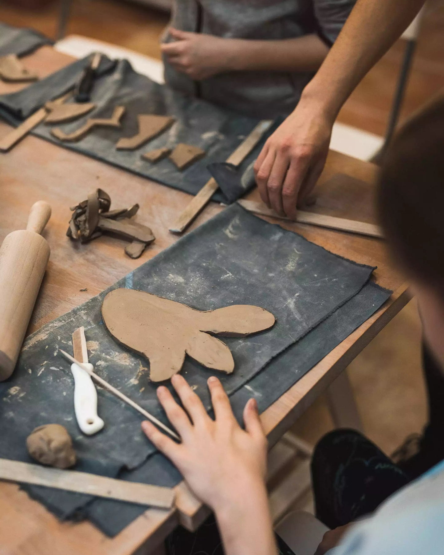 Stół w trakcie warsztatów, a na nim glina oraz materiały do lepienia takie jak wałek, drewniane listewki, nożyk i ściereczki