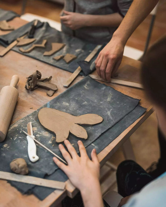 Stół w trakcie warsztatów, a na nim glina oraz materiały do lepienia takie jak wałek, drewniane listewki, nożyk i ściereczki