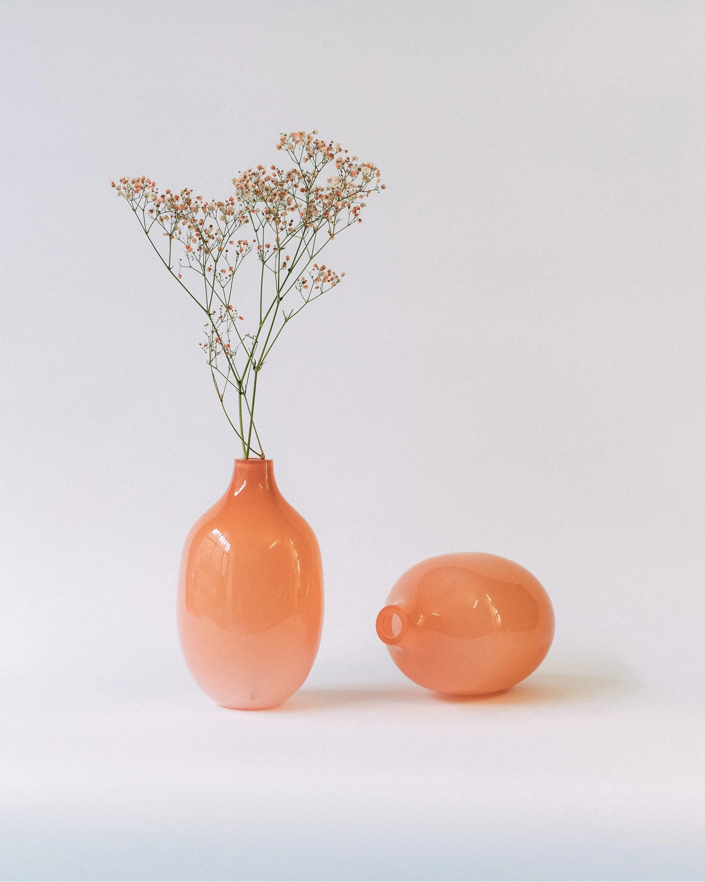 Kompozycja z kwiatami dwóch szklanych wazonów Ganna Glass w kolorze brzoskwiniowym na jasnym tle - szkło artystyczne, minimalistyczny design