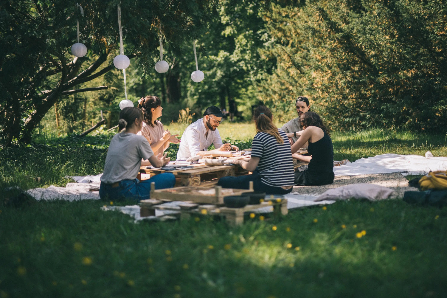 Grupa kilku osób siedzi na trawie w parku i pracuję nad ceramiką