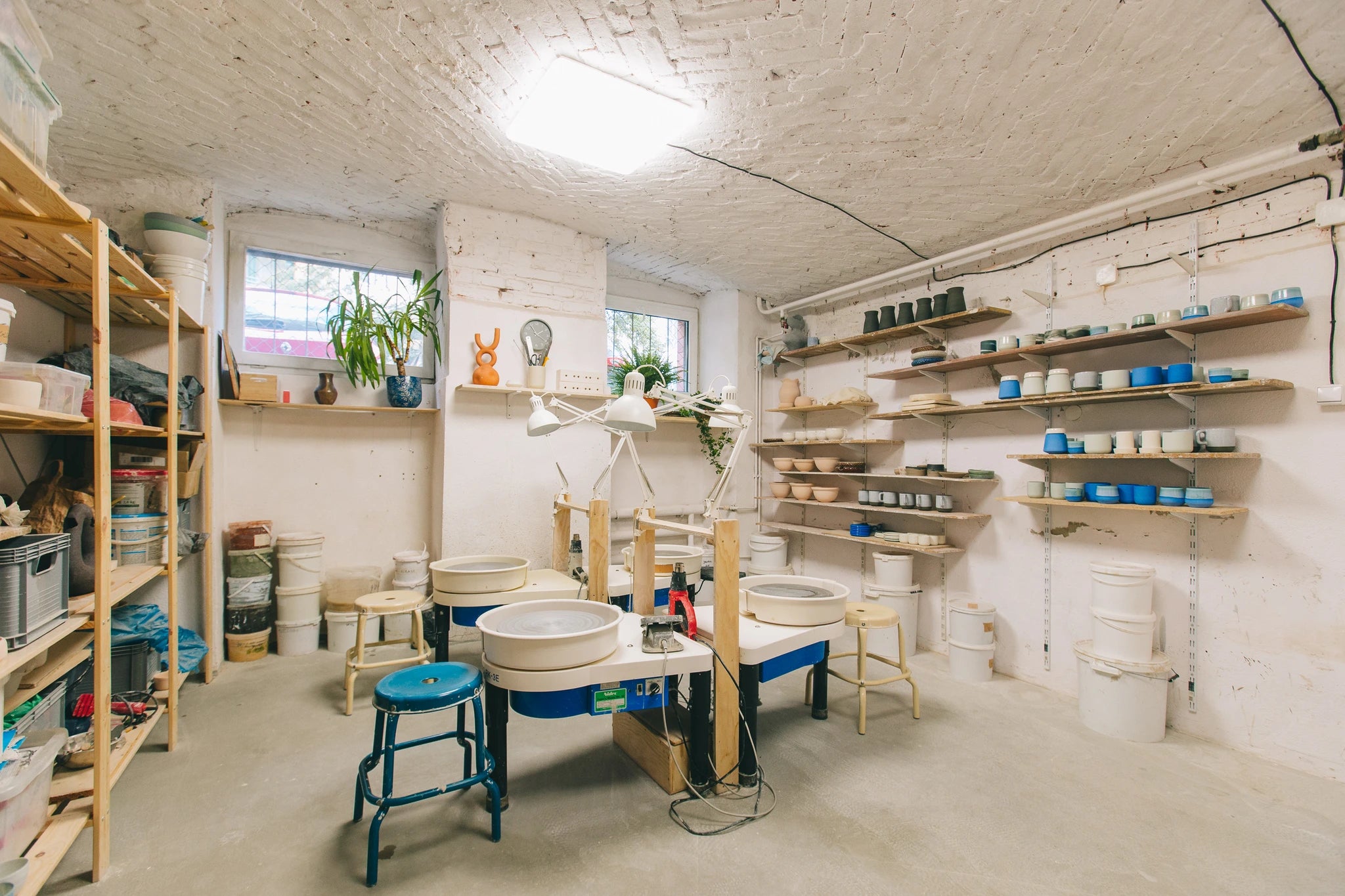 Wnętrze pracowni z kołami garncarskimi i półkami na przechowywanie gotowych prac