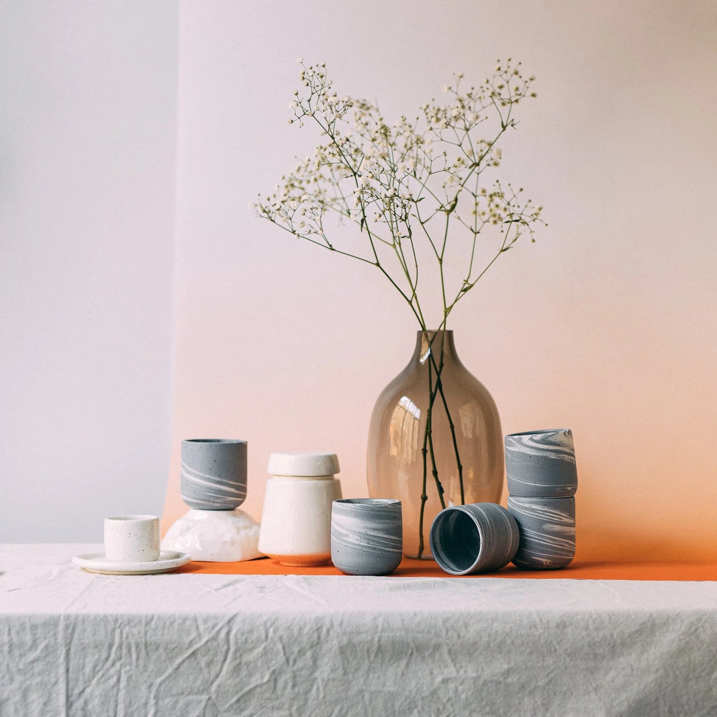 Kompozycja ręcznie robionych ceramicznych kubków i misek z marmurkowaniem obok szklanego wazonu  - voucher uniwersalny Zakwas Studio