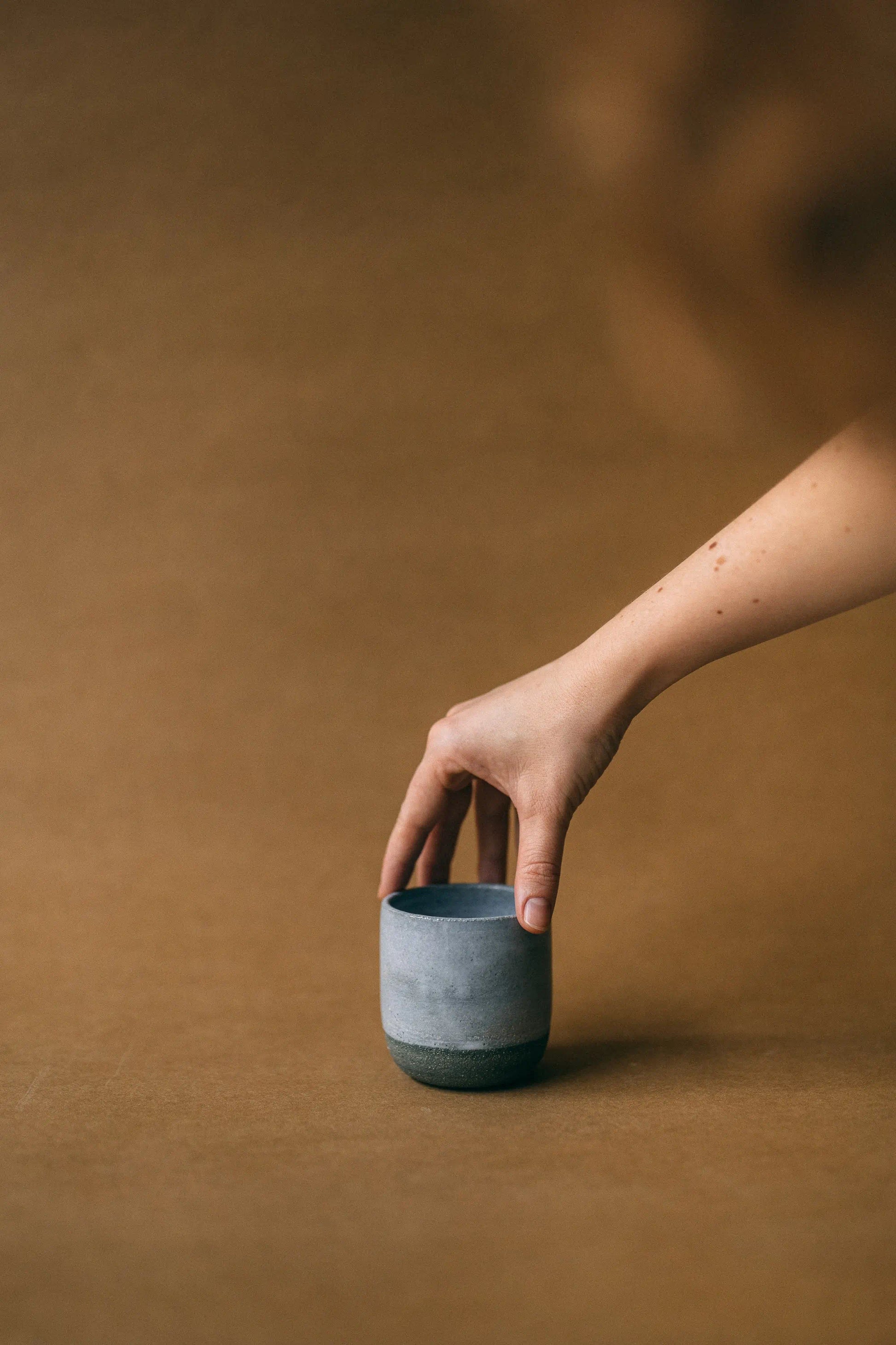 Dłoń ustawiająca ceramiczną, grafitową czarkę z zestawu do kawy